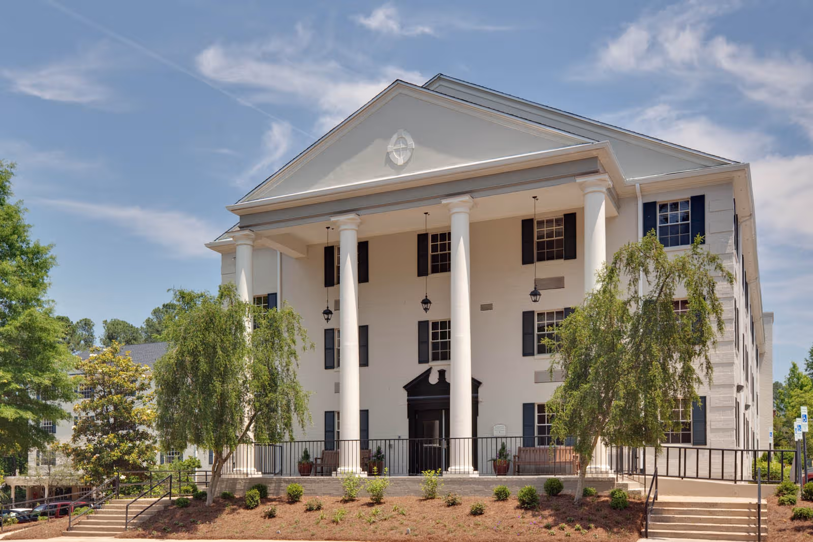 White, columned senior living building with a peaked roof and landscaped front lawn.