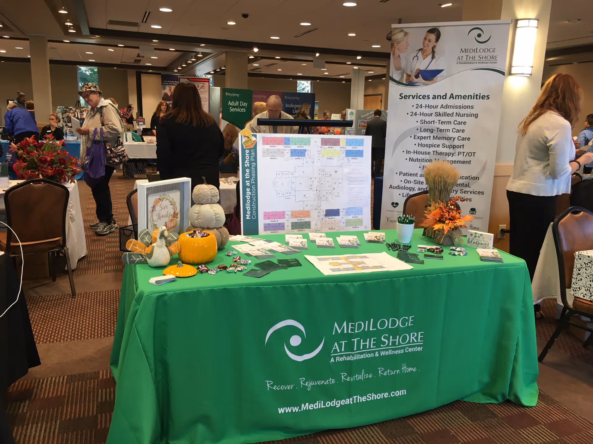 Indoor expo booth for Medilodge at the Shore with a green table and attendees.