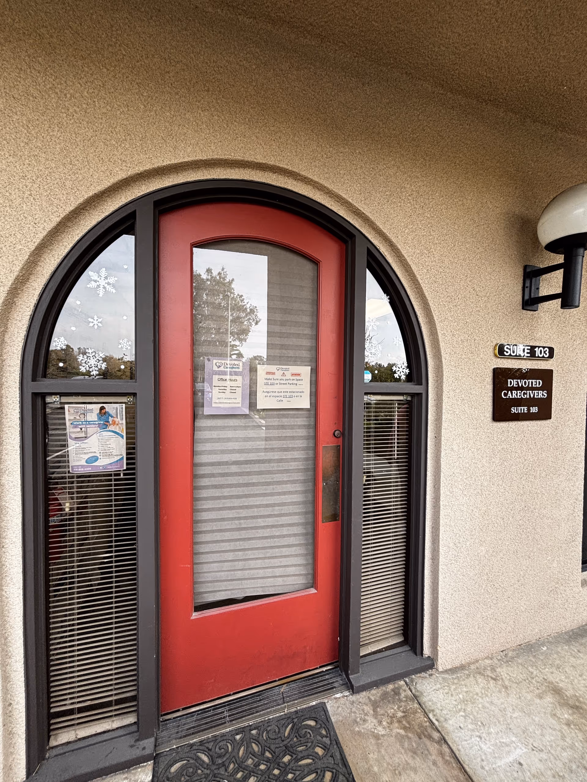 Red arched door with windows, beige exterior, and a sign reading Devoted Caregivers Suite 103.