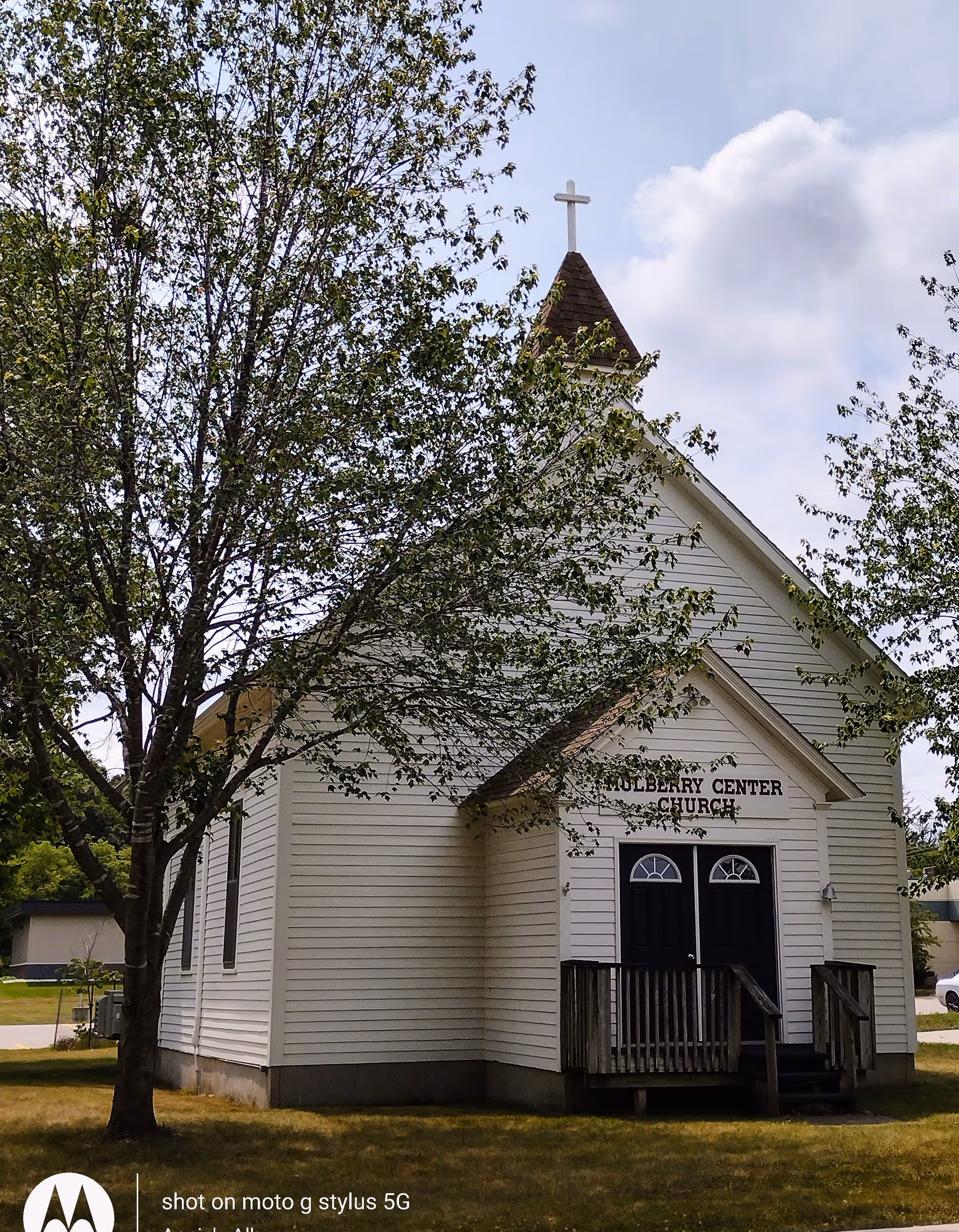 White church-like building with a cross-topped steeple beside trees.