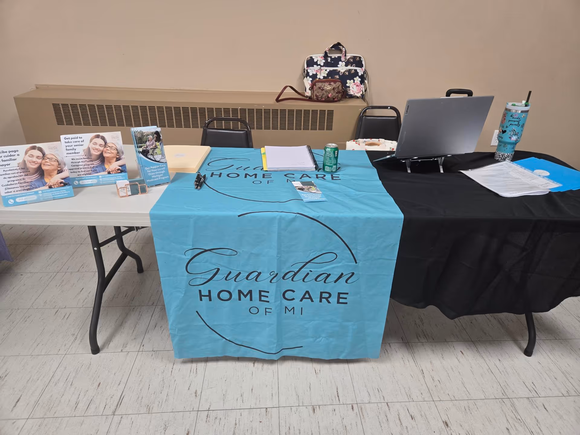 A booth with Guardian Home Care of MI banner, laptop, and brochures indoors.
