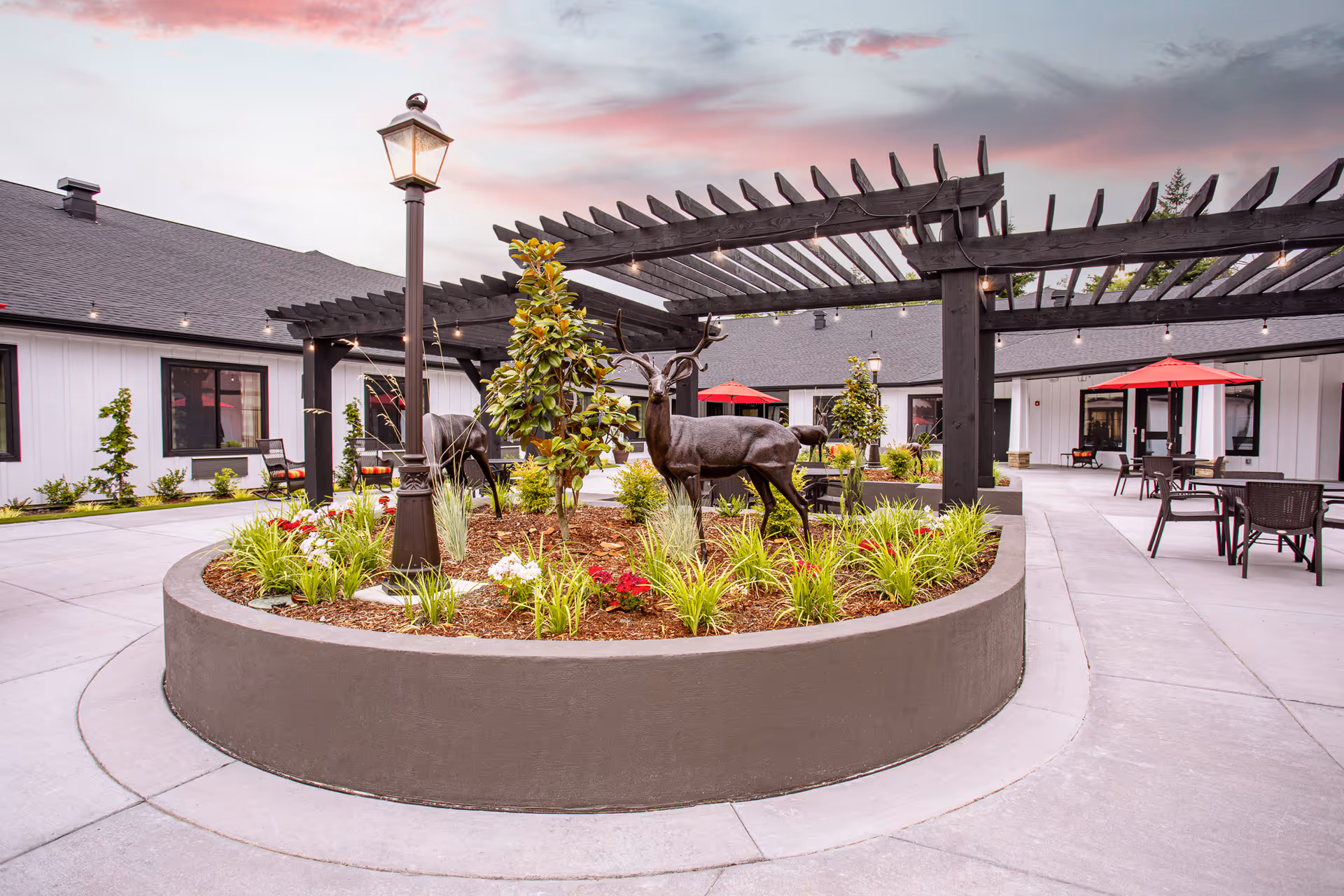 Outdoor memory care courtyard with a circular planter, deer sculptures, and seating under a pergola.