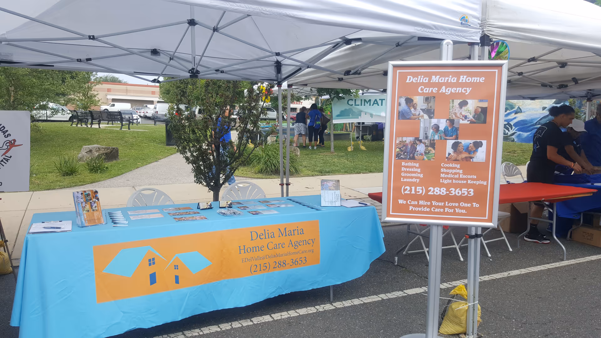 Outdoor booth for Delia Maria Home Care Agency with turquoise tablecloth and orange sign