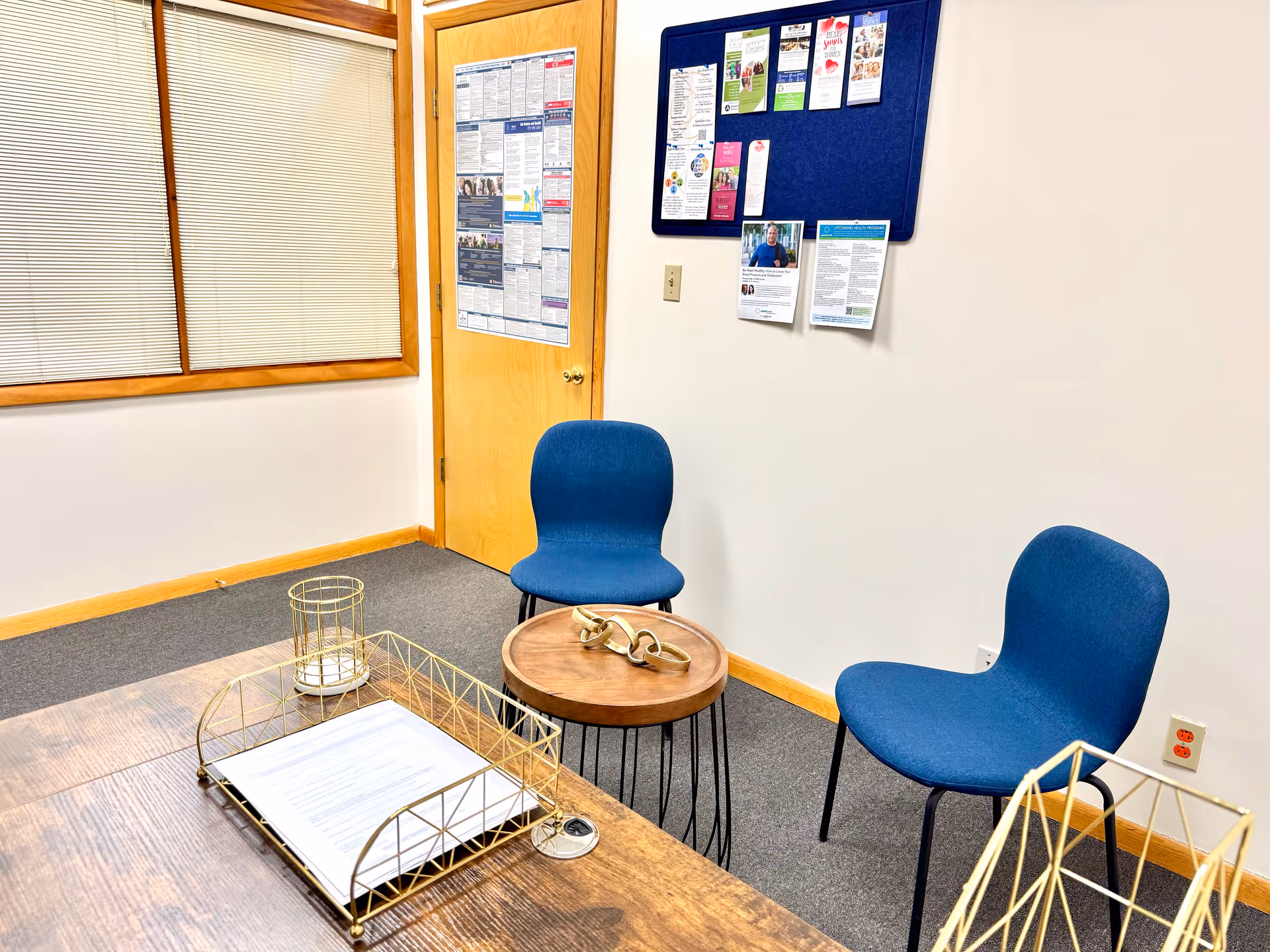 A small interior waiting area with blue chairs, a wooden table, and bulletin boards.