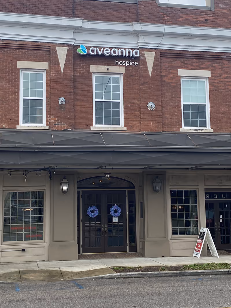 Brick building with Aveanna hospice sign and glass double doors at the entrance.