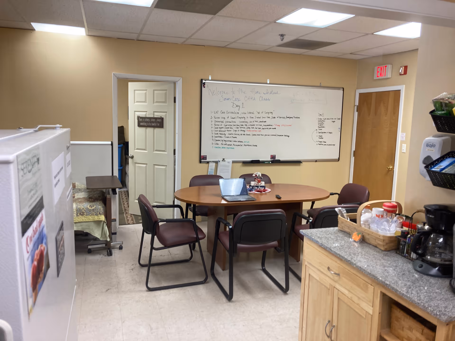 Small conference room with round wooden table, chairs, whiteboard, and kitchenette area