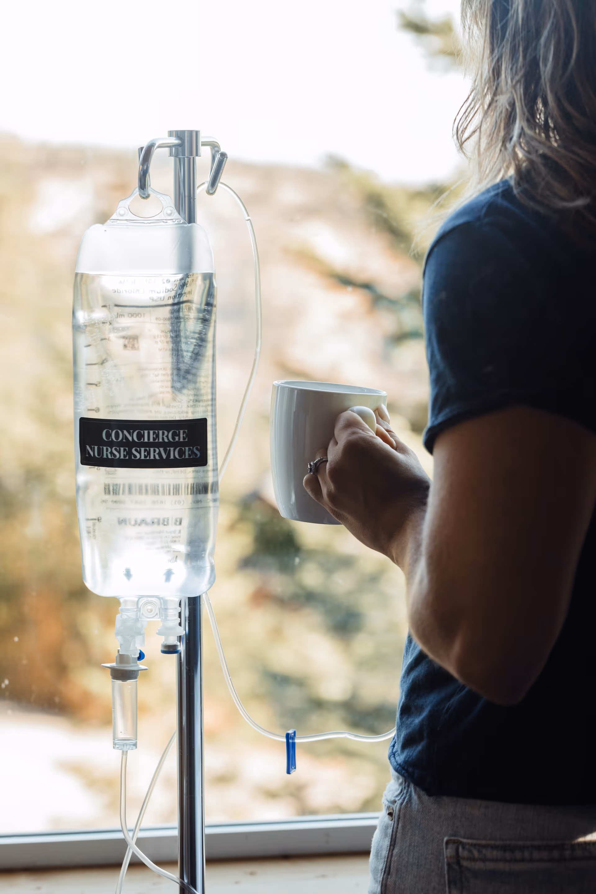 IV infusion stand labeled Concierge Nurse Services beside a person holding a mug indoors