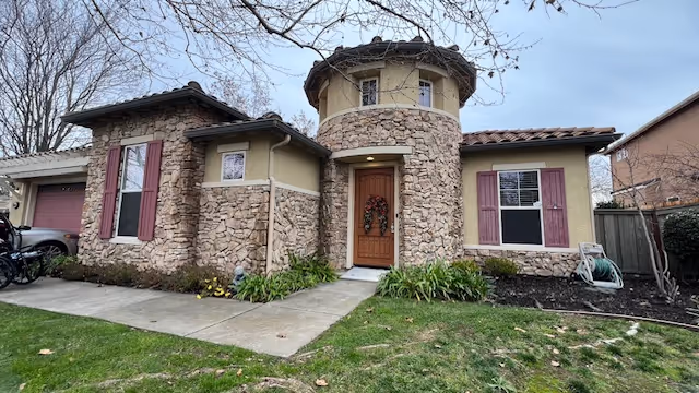 Stone-clad villa with rounded tower, front door wreath, and manicured lawn.