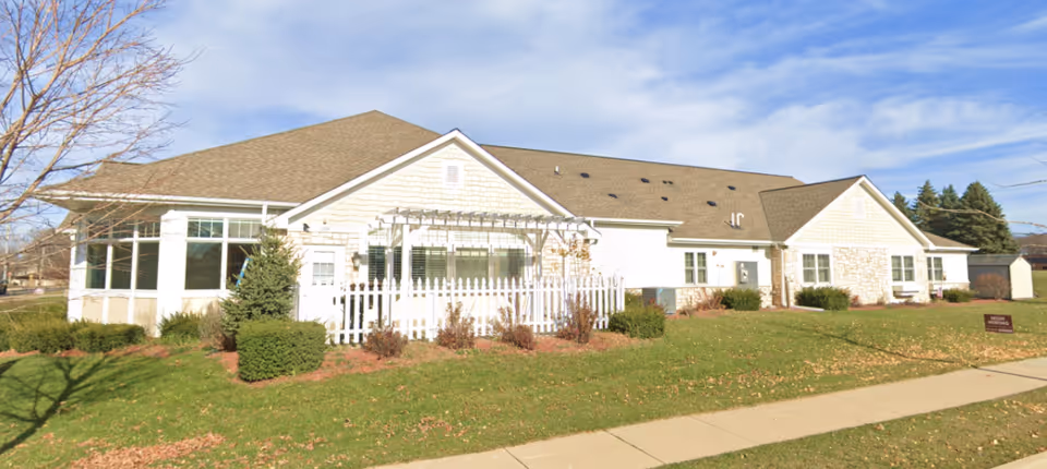 Single story senior living facility with siding, white trim, a white picket fence, and manicured lawn.
