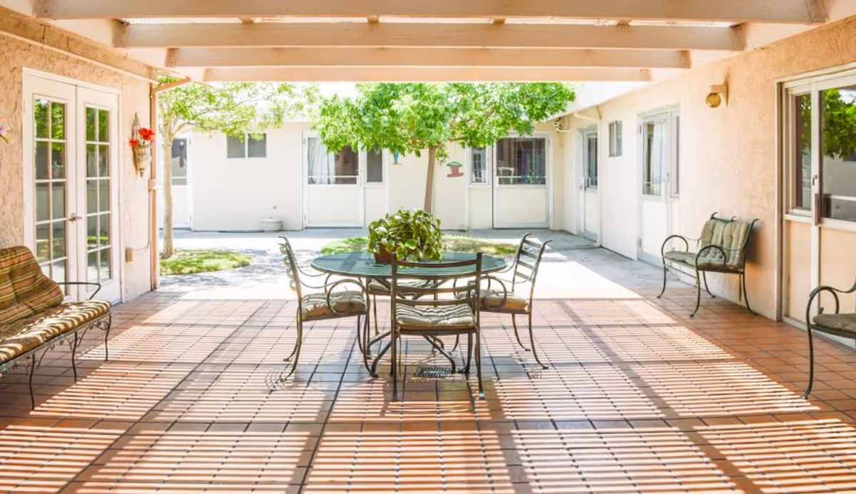 Covered courtyard patio with metal furniture and greenery, doors to resident rooms.