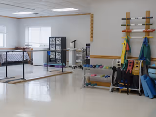 Physical therapy room with parallel bars, weights, and rehab equipment.