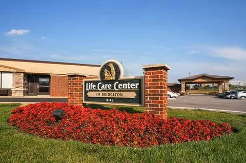 Front view of Life Care Center of Bridgeton sign with red flowers and parking lot.