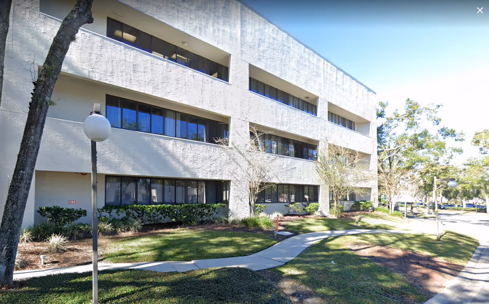 Exterior view of a white multi-story senior living building with a paved walkway and landscaping.