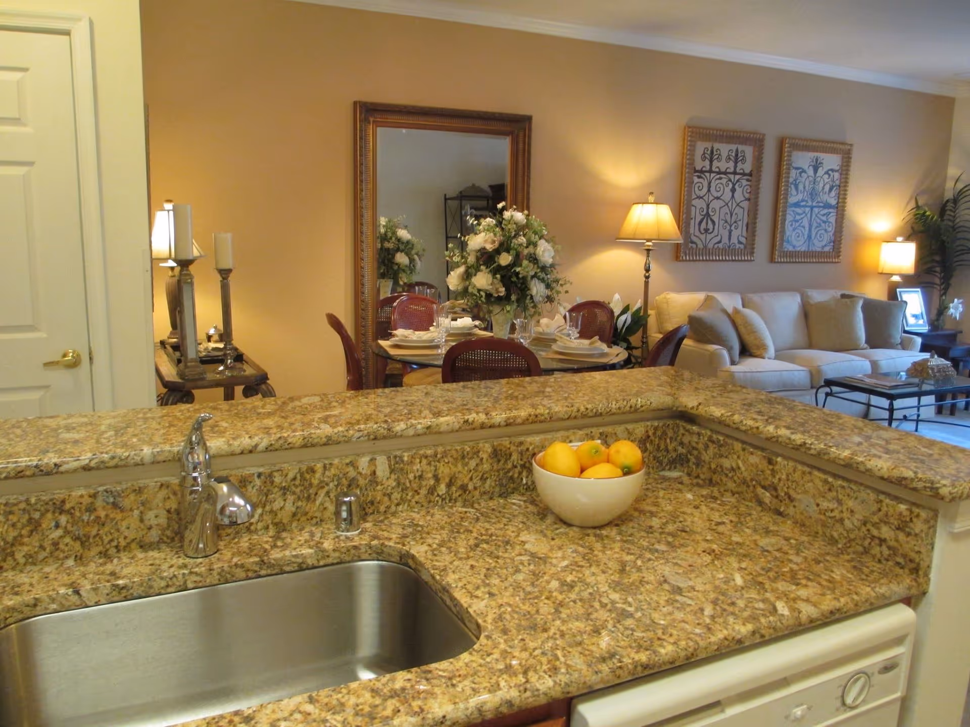 Granite kitchen counter opens to a dining area and living room with lamps.