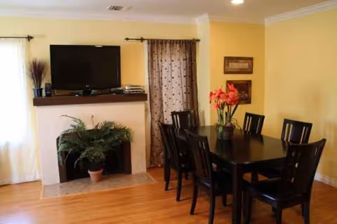 Dining room with a rectangular table, six dark wood chairs, TV on a mantel.