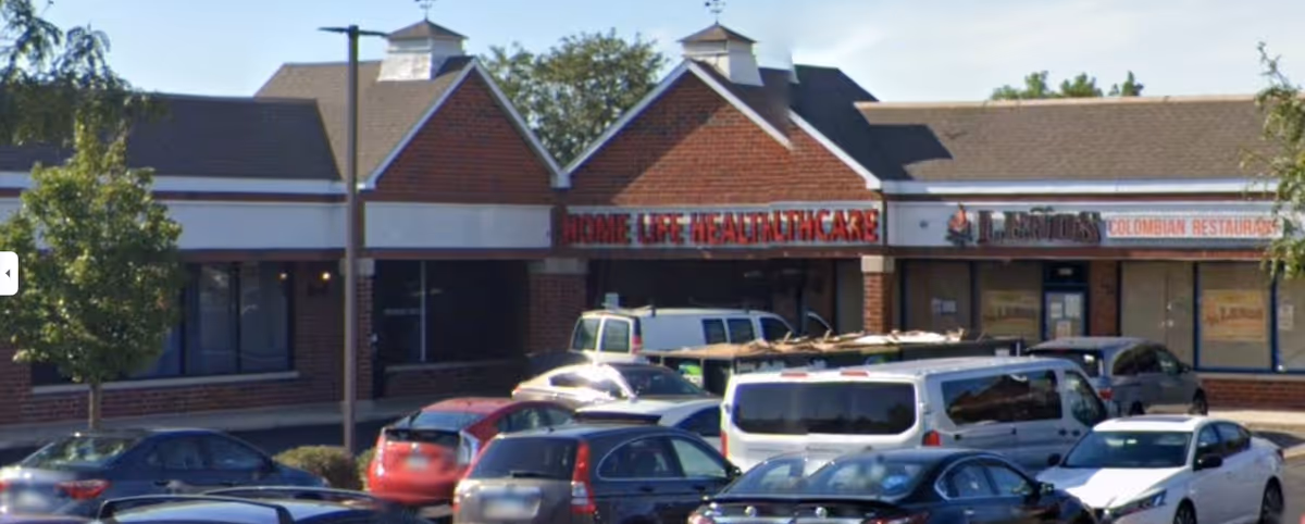Exterior of a strip mall with Home Life Healthcare signage and several parked cars.
