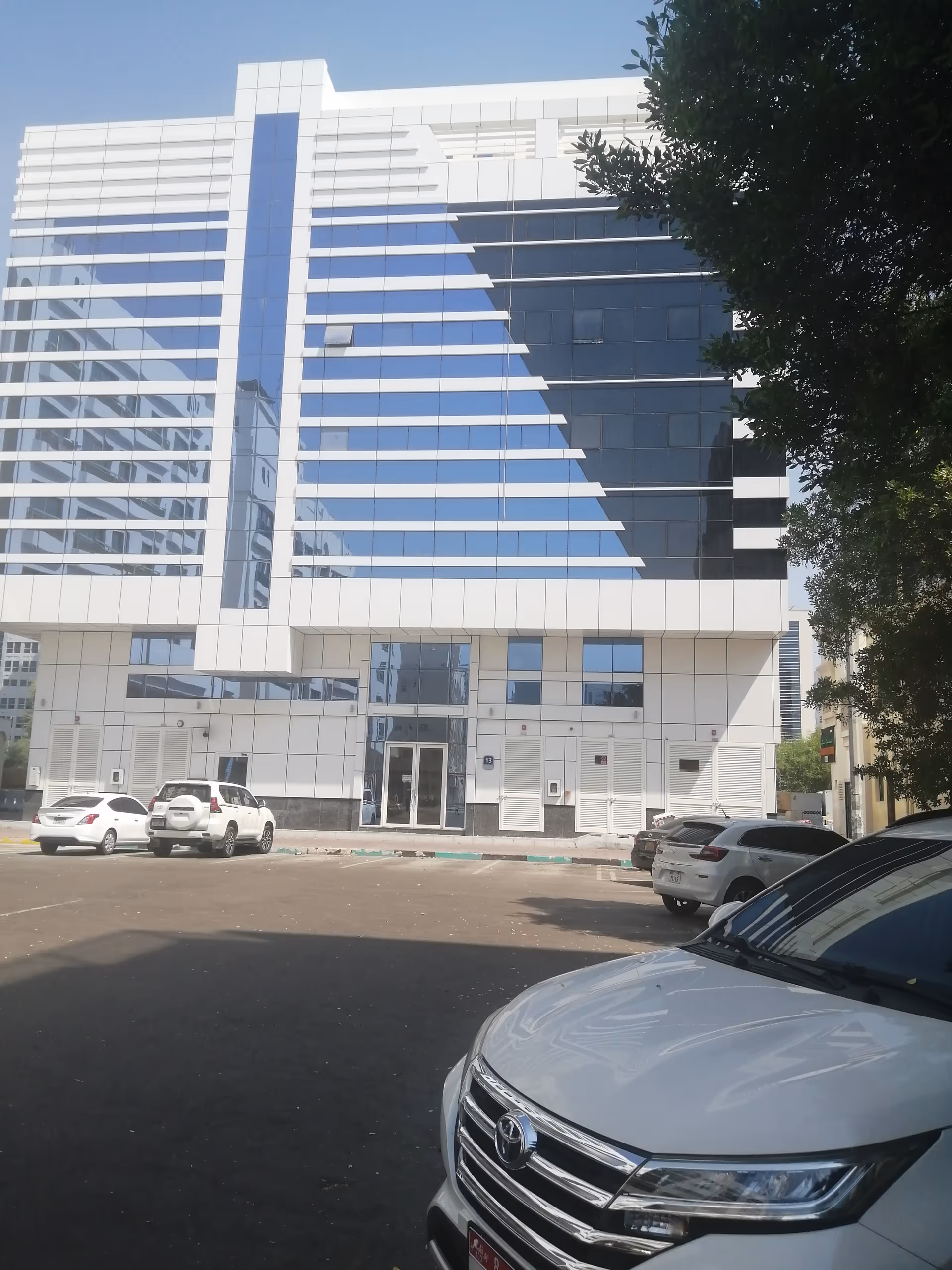 Modern glass-front building with white and blue panels and parked cars in front.