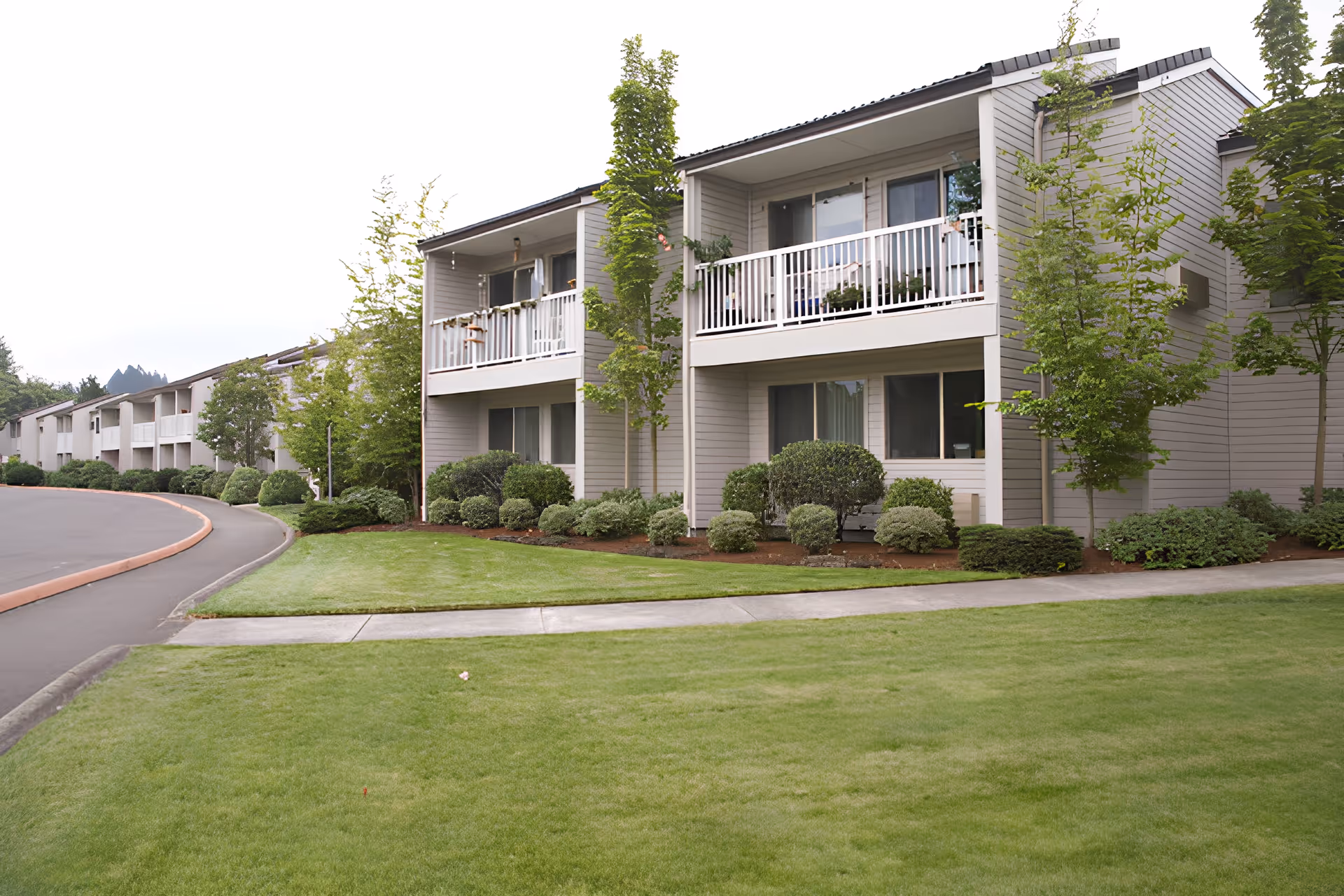 Two-story retirement community building with balconies, landscaped shrubs, and a manicured lawn.