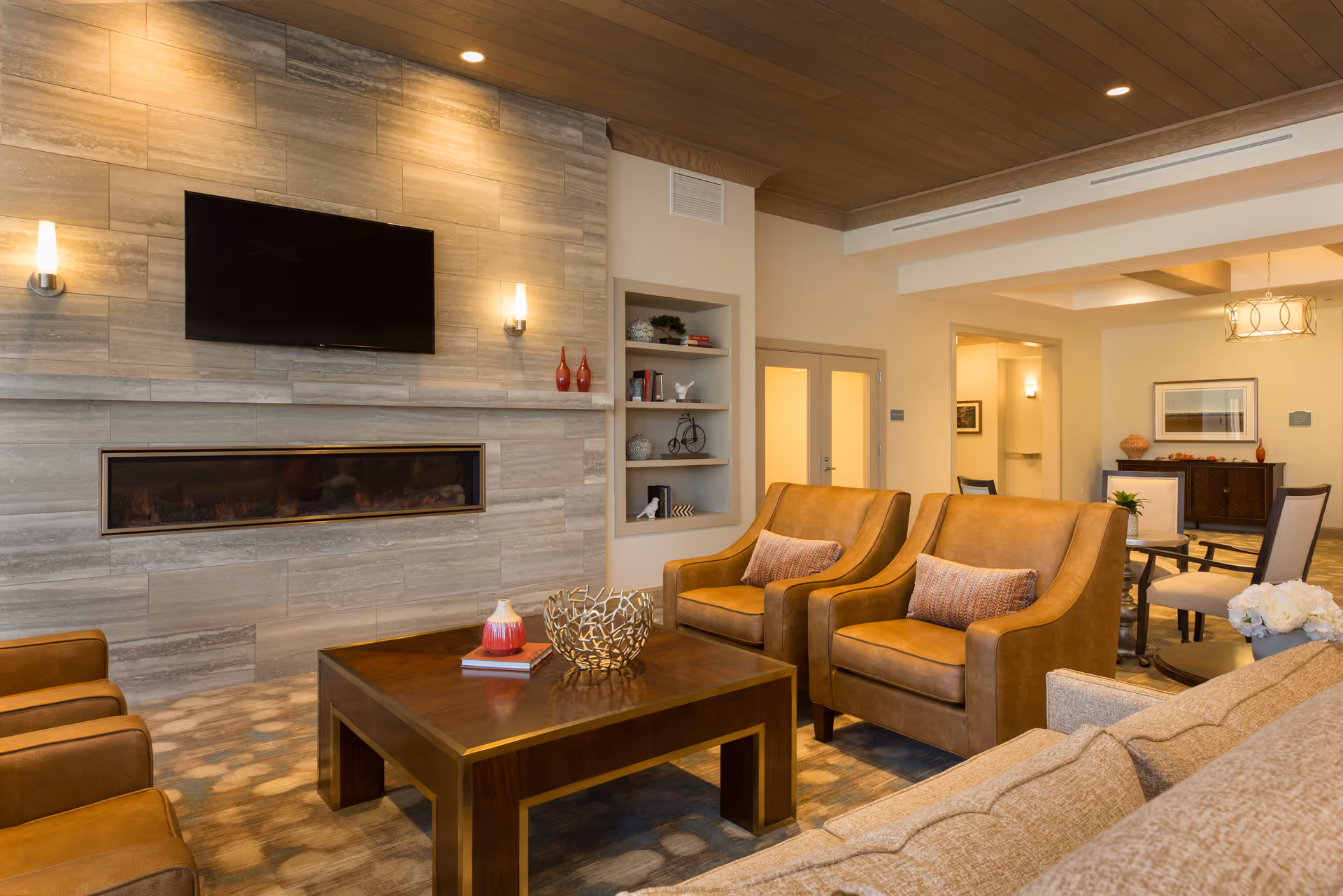 A cozy communal living room with leather armchairs, a wooden coffee table, a linear fireplace and a wall-mounted TV.