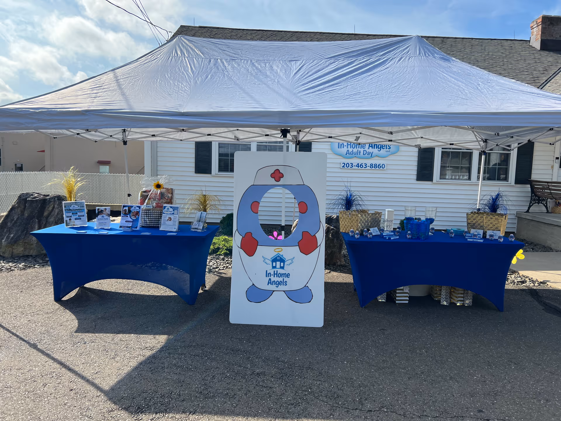 Outdoor promotional setup under a white canopy with blue tables for In-Home Angels.
