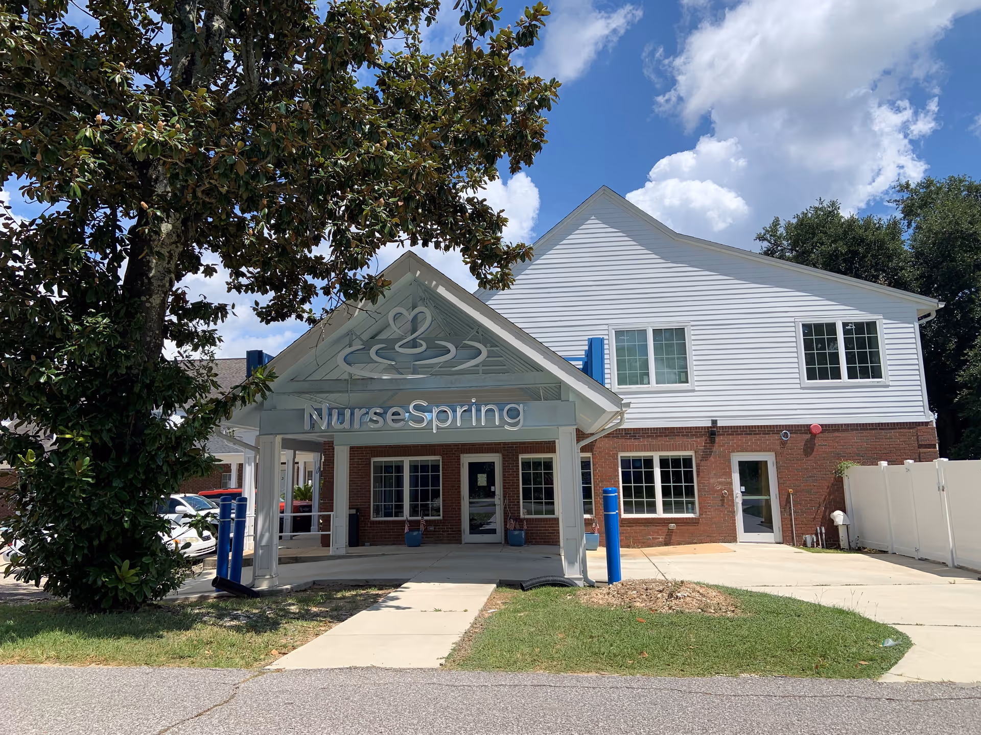 Front view of NurseSpring facility with white siding, brick base, and blue entrance pillars.