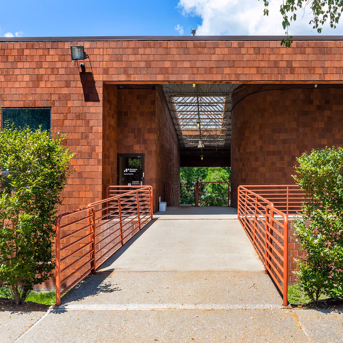 Brick building entrance with red metal railings and a glass skylight walkway.