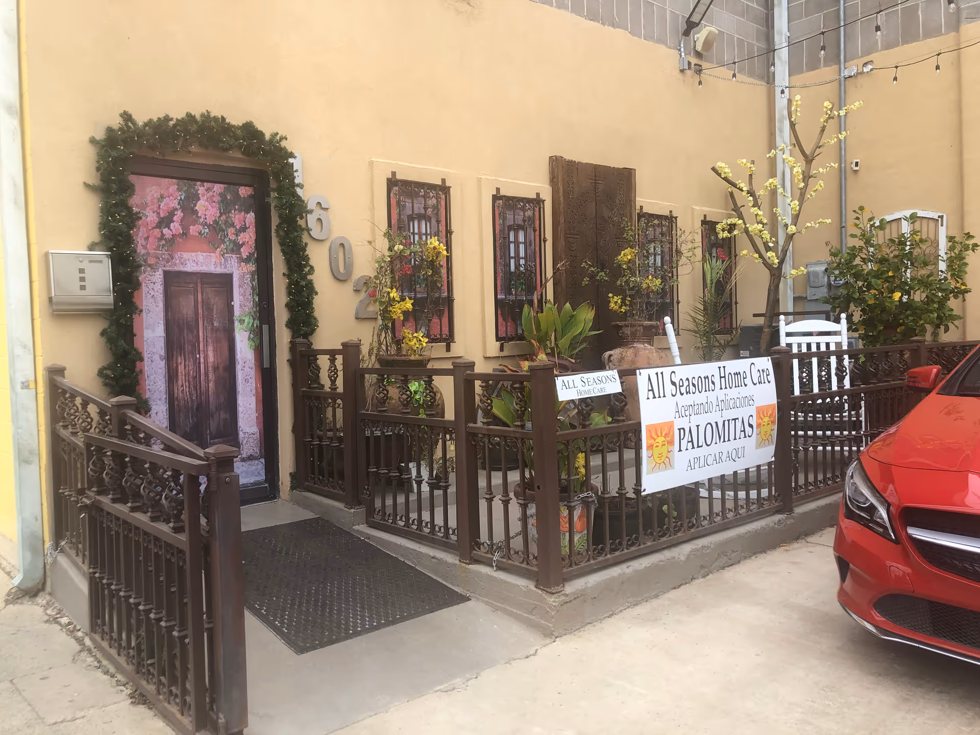 Exterior courtyard with railing, plants, banners, and a red car outside All Seasons Home Care.