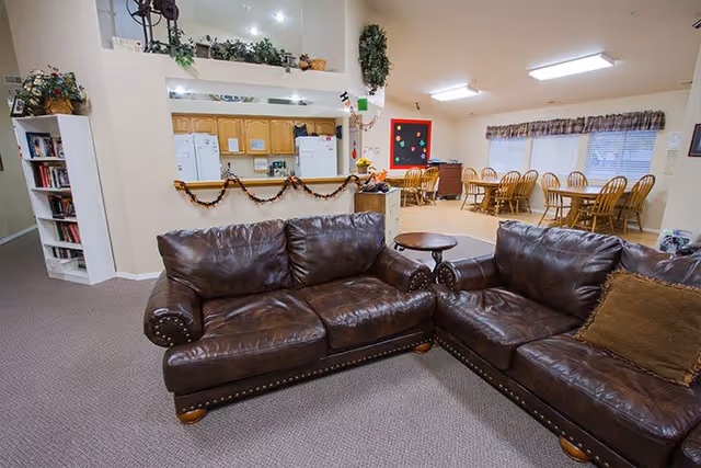 A communal living area with two brown leather sofas and a small table in front of a dining area and kitchen pass-through.