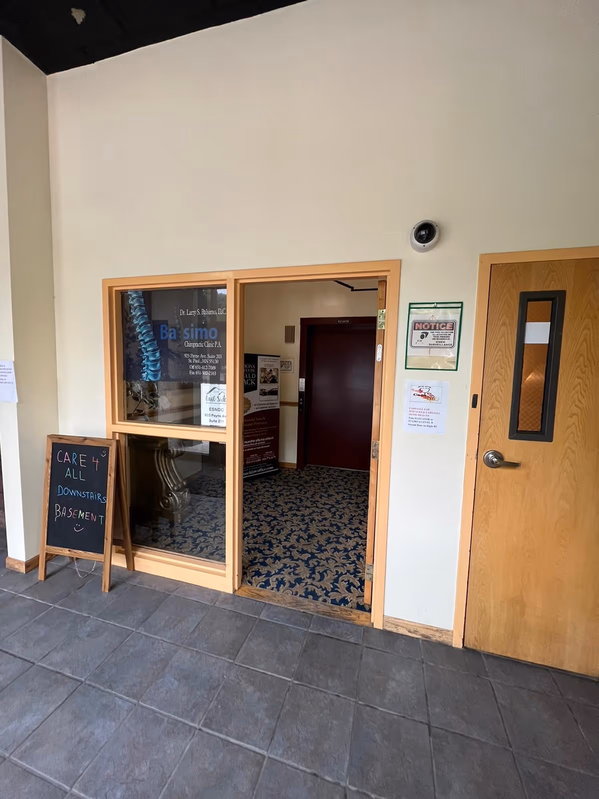 Interior entrance with glass door, chalkboard sign, and carpeted basement hallway.