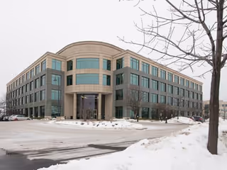 Modern glass-front building with curved entrance in a snowy parking lot.