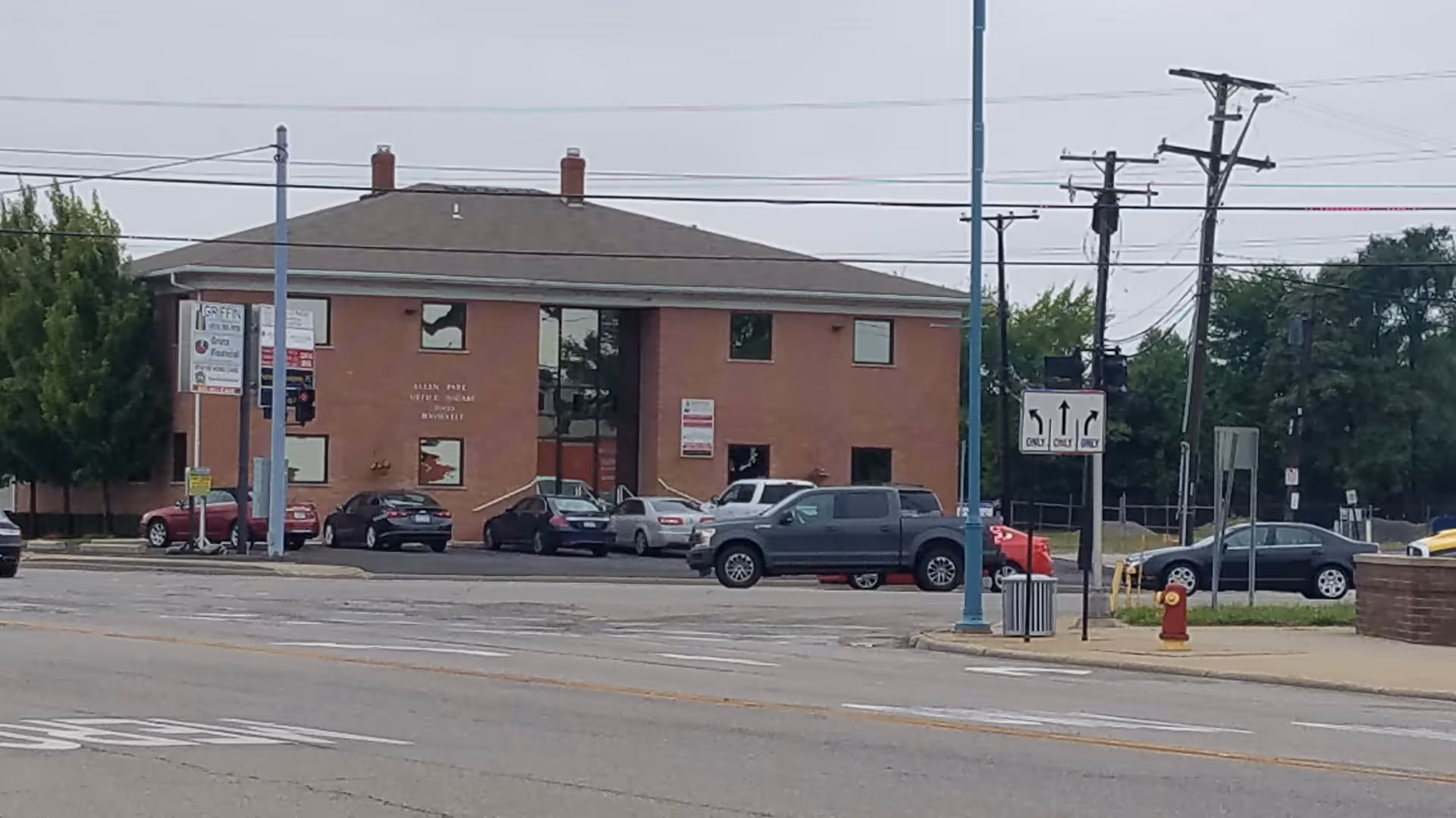 Brick two-story care facility with parked cars along a street and utility poles.