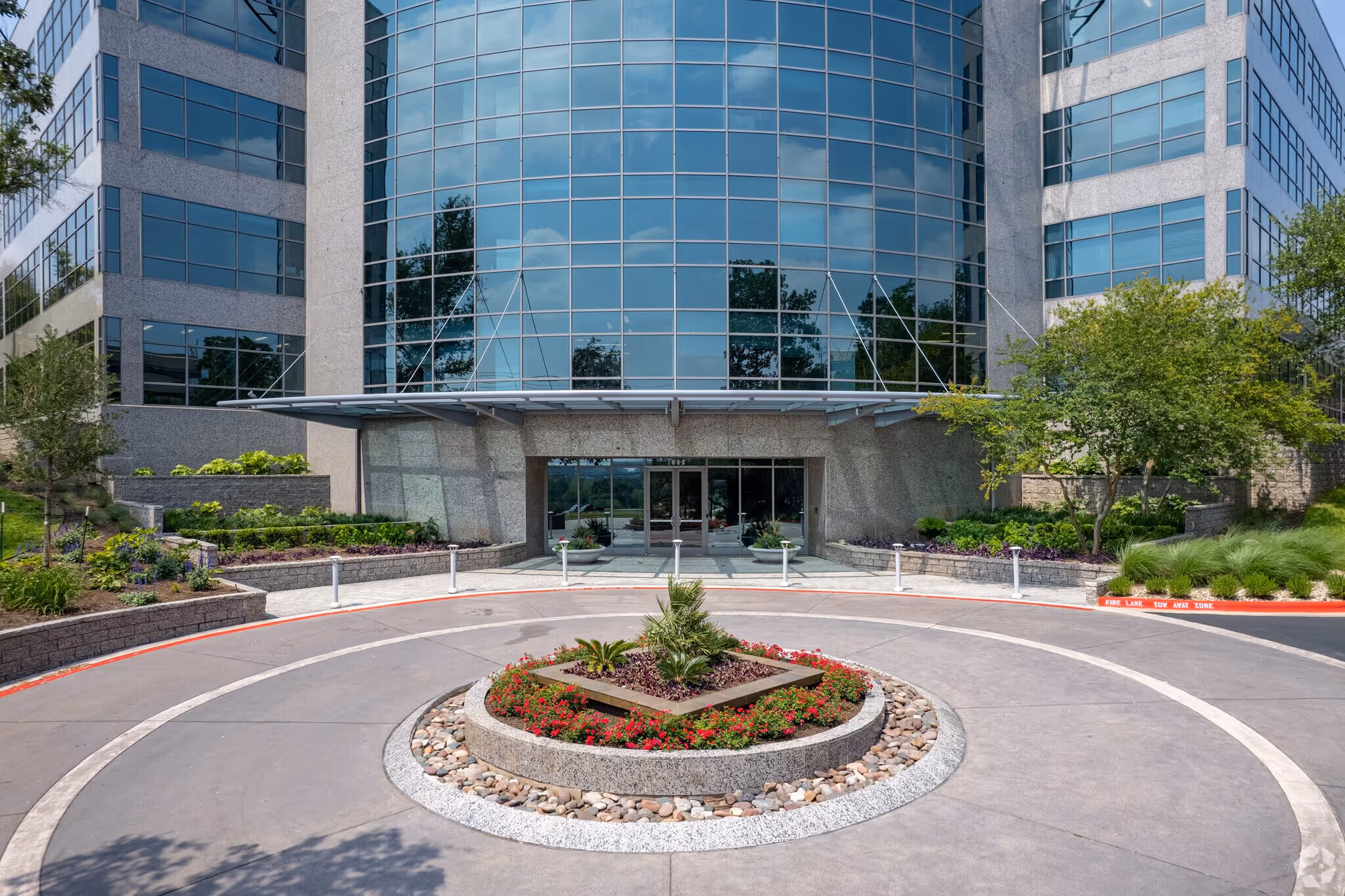 Front view of a modern glass-front building with a circular driveway and landscaped island.
