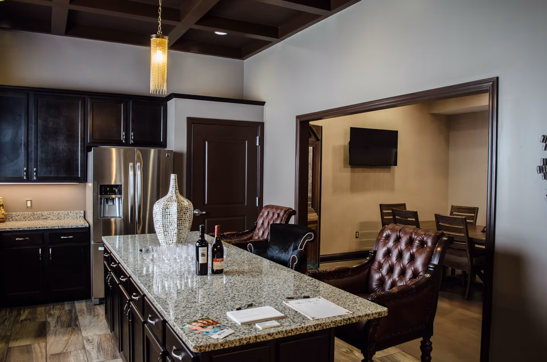 A stylish kitchen with a granite island, leather armchairs, stainless steel refrigerator and an adjoining dining area with a wall-mounted TV.