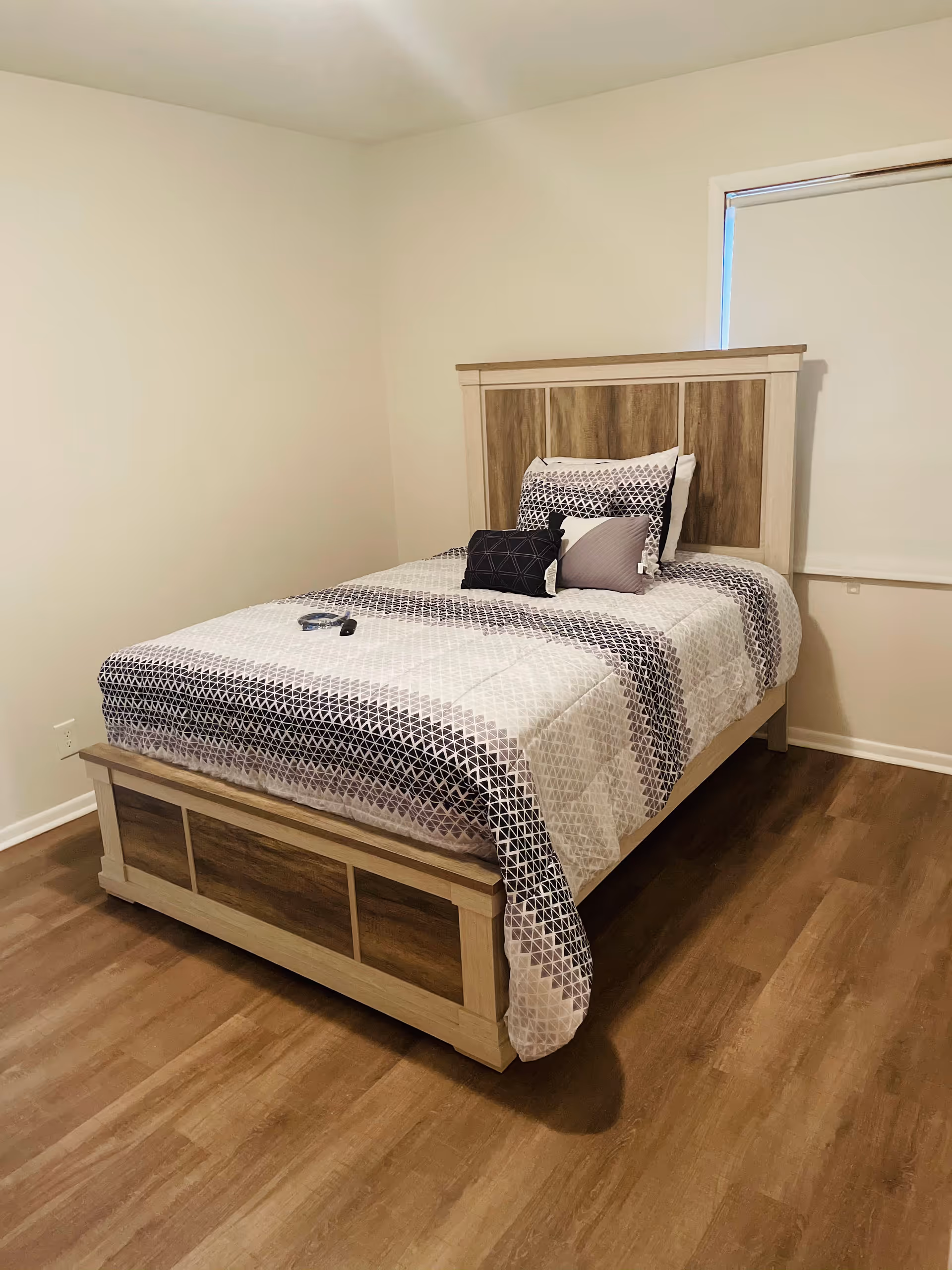 A neatly made bedroom with a wooden bed frame and patterned quilt.