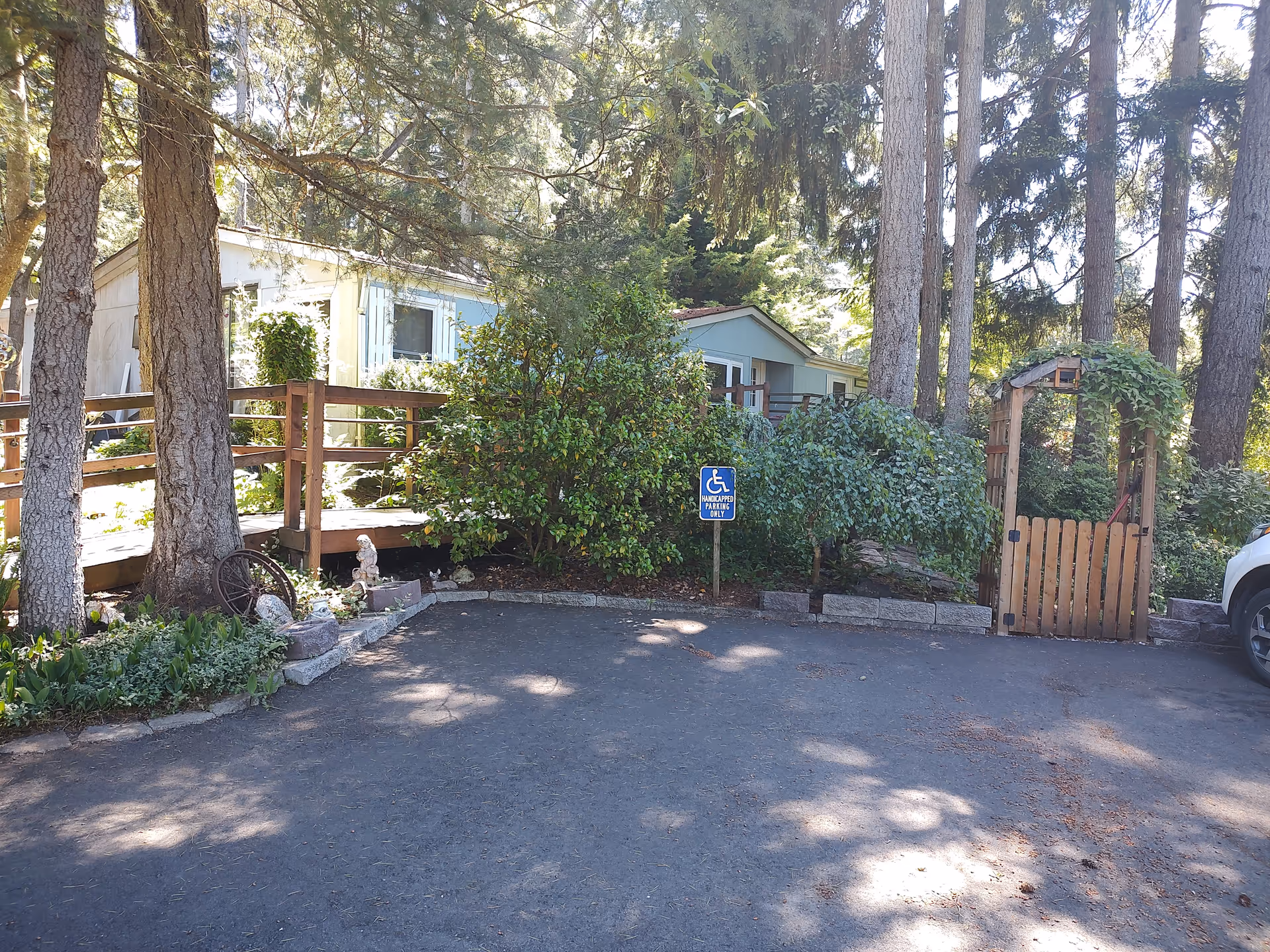 Exterior view of a care home with trees, wooden fence, gate, handicap sign, and parking area.