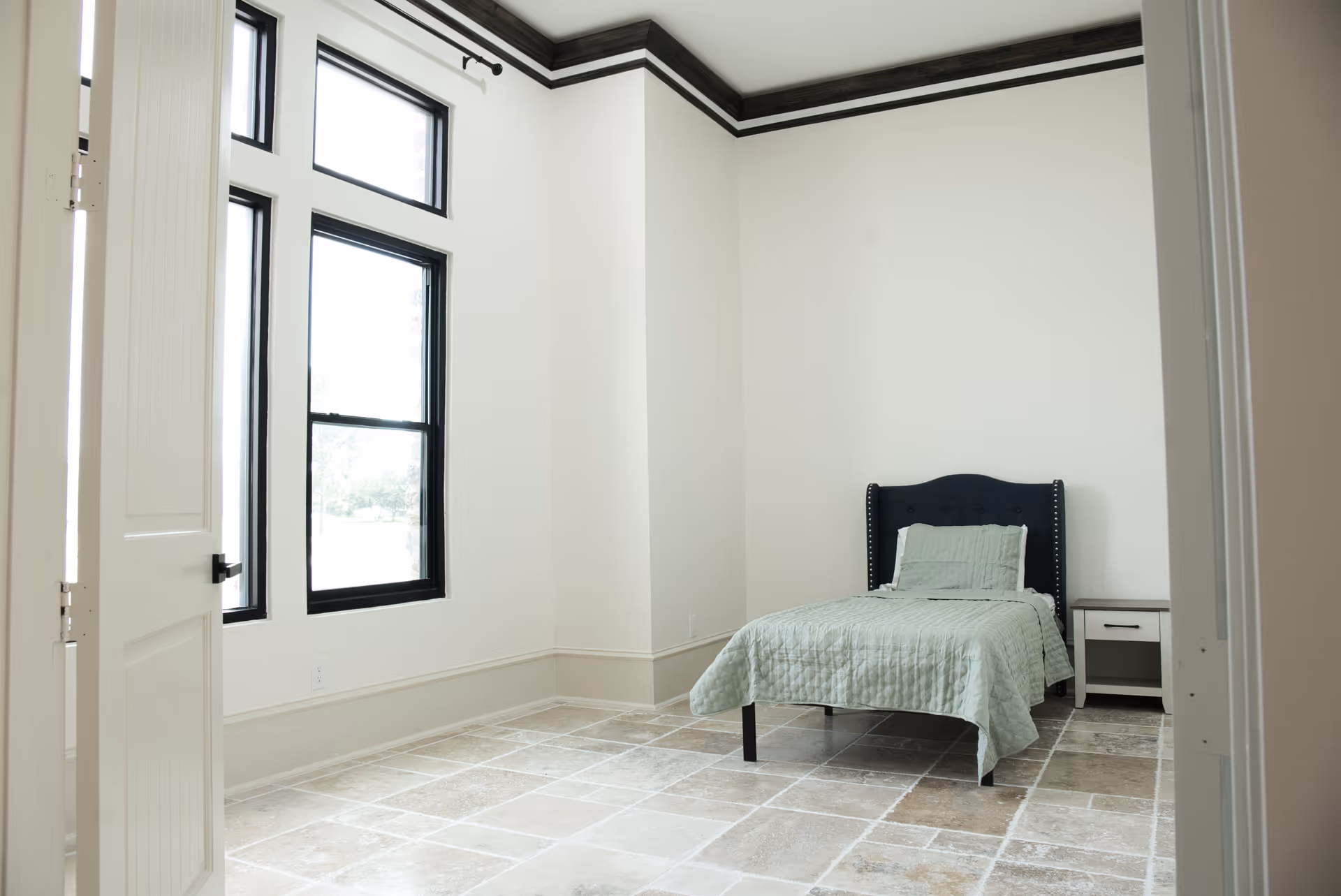 A minimal bedroom with a single bed, nightstand, and large windows.