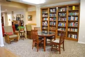 Cozy common room with a round wooden table, surrounding chairs, and tall bookshelves.