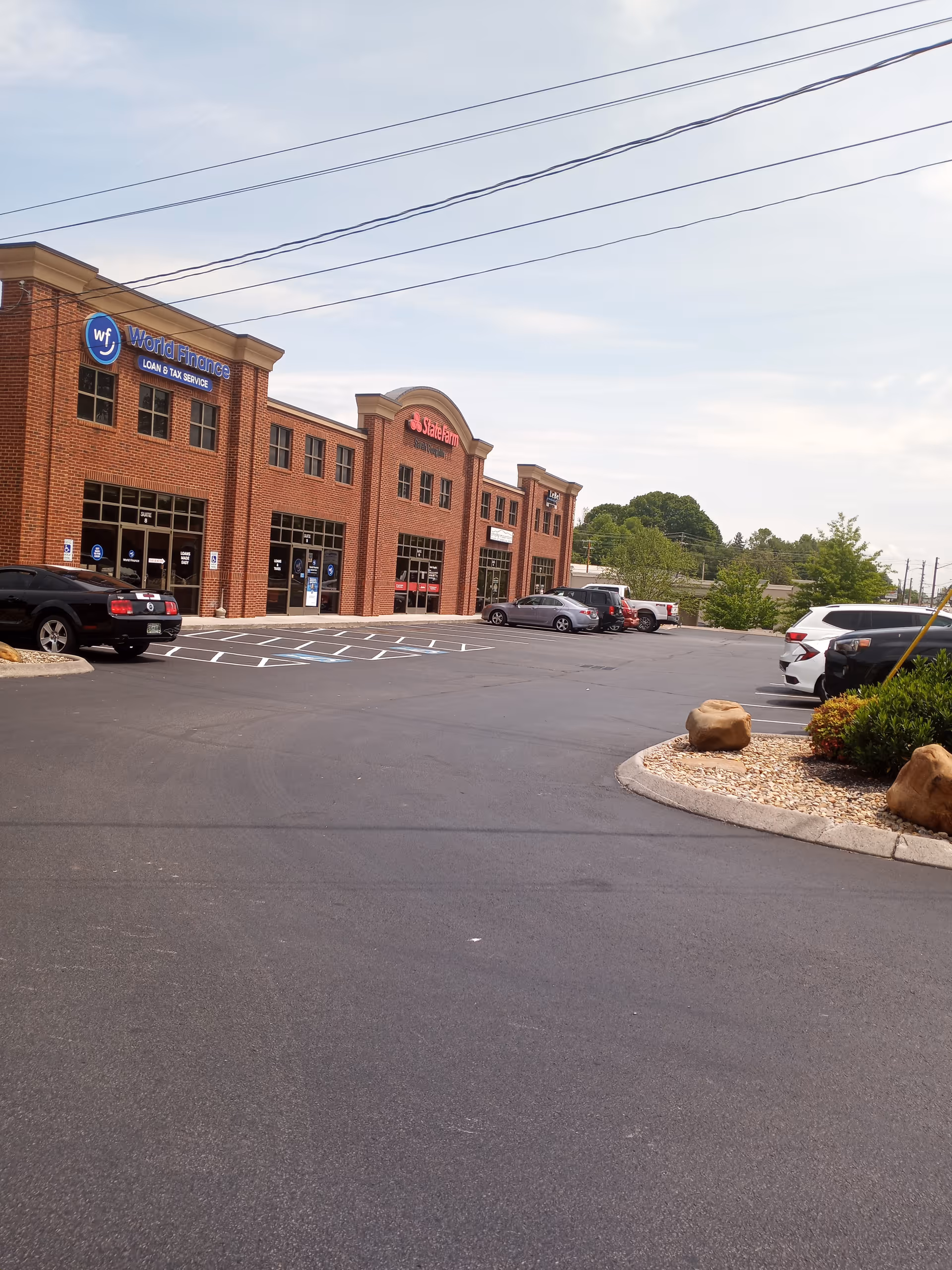 A brick storefront strip mall with parked cars and a spacious parking lot.