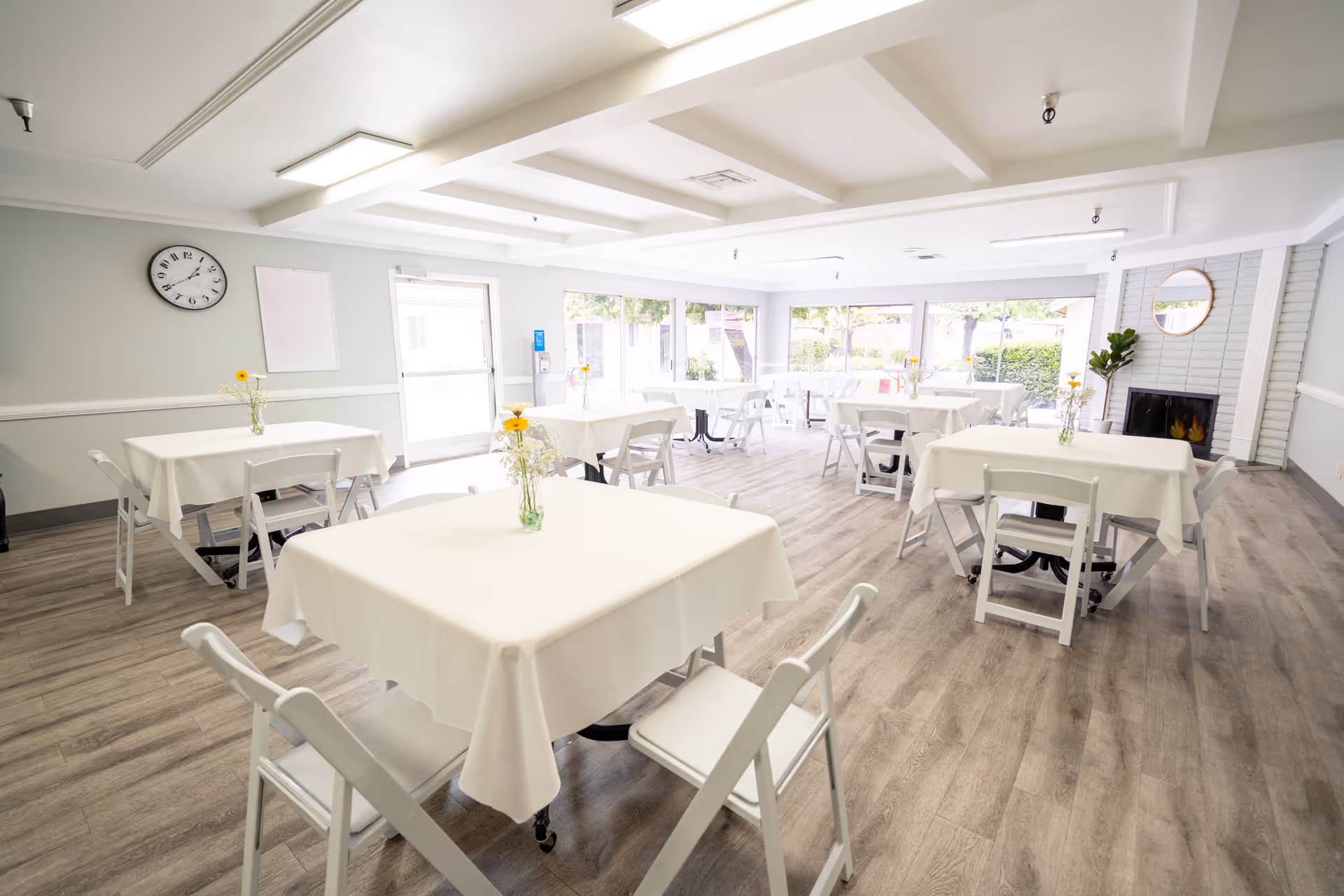 Bright airy dining room with white tables, chairs, and a fireplace in Buena Vista Care Center.