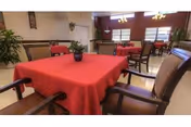 Dining room with red-covered tables and wooden chairs in a senior facility.