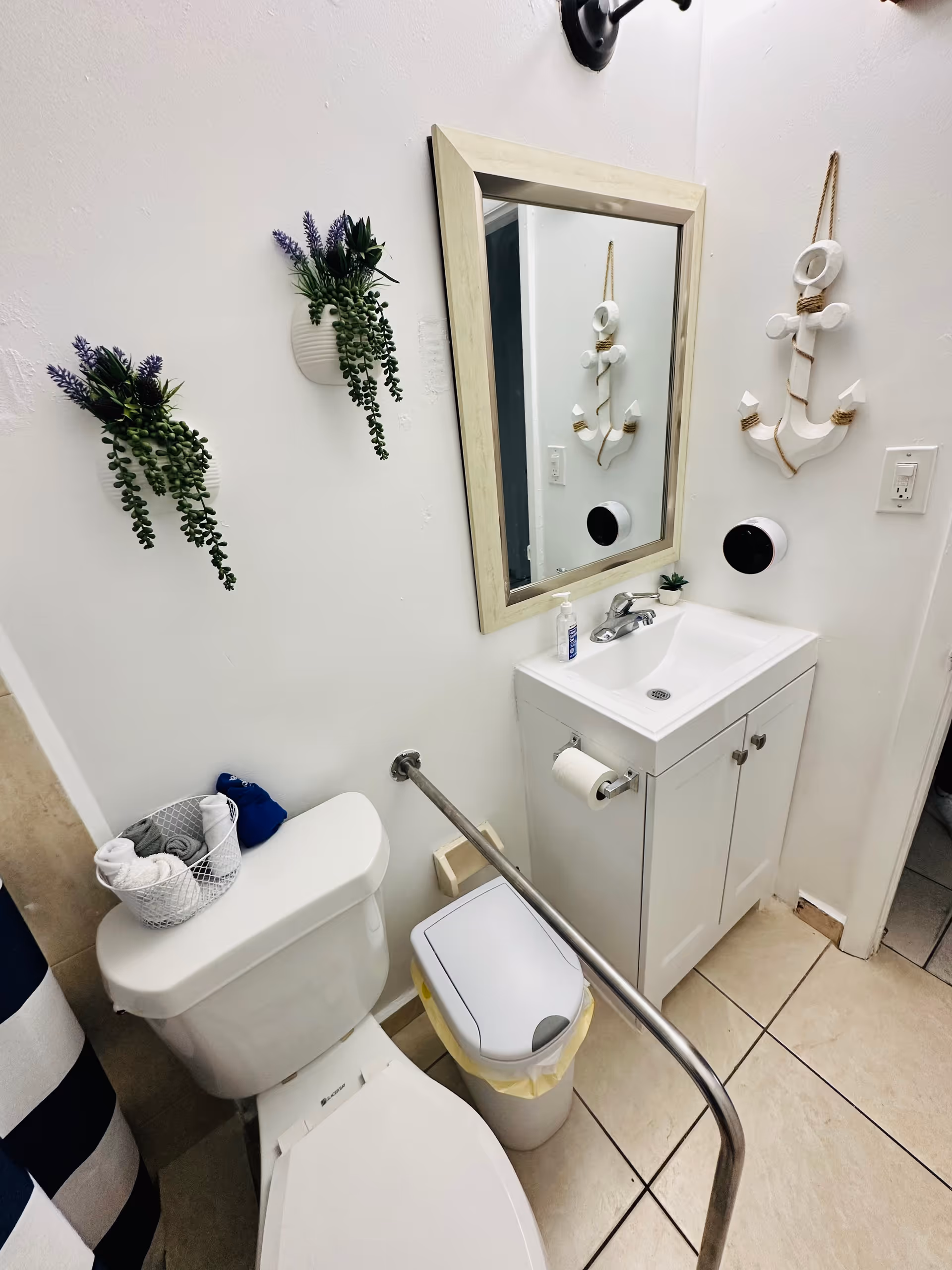 Small bathroom with toilet, sink, mirror, plants, and a grab bar.