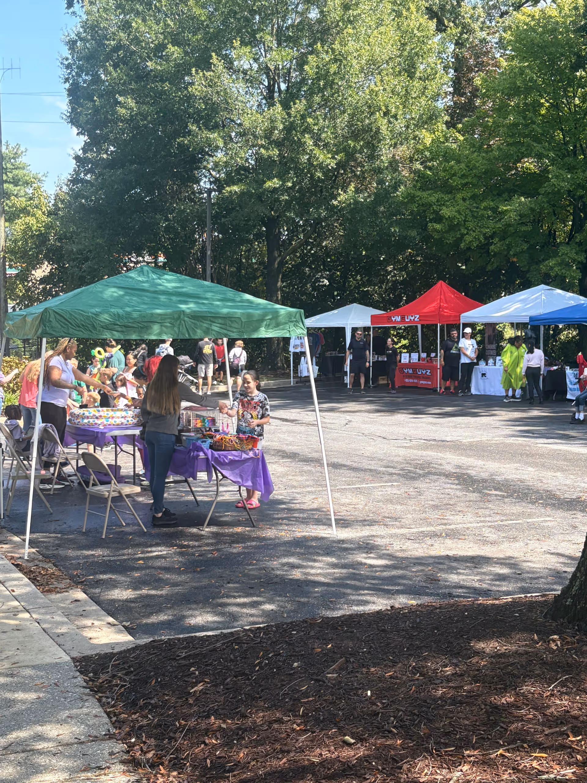 Outdoor community fair with colorful tents, tables, and people engaging under shade.