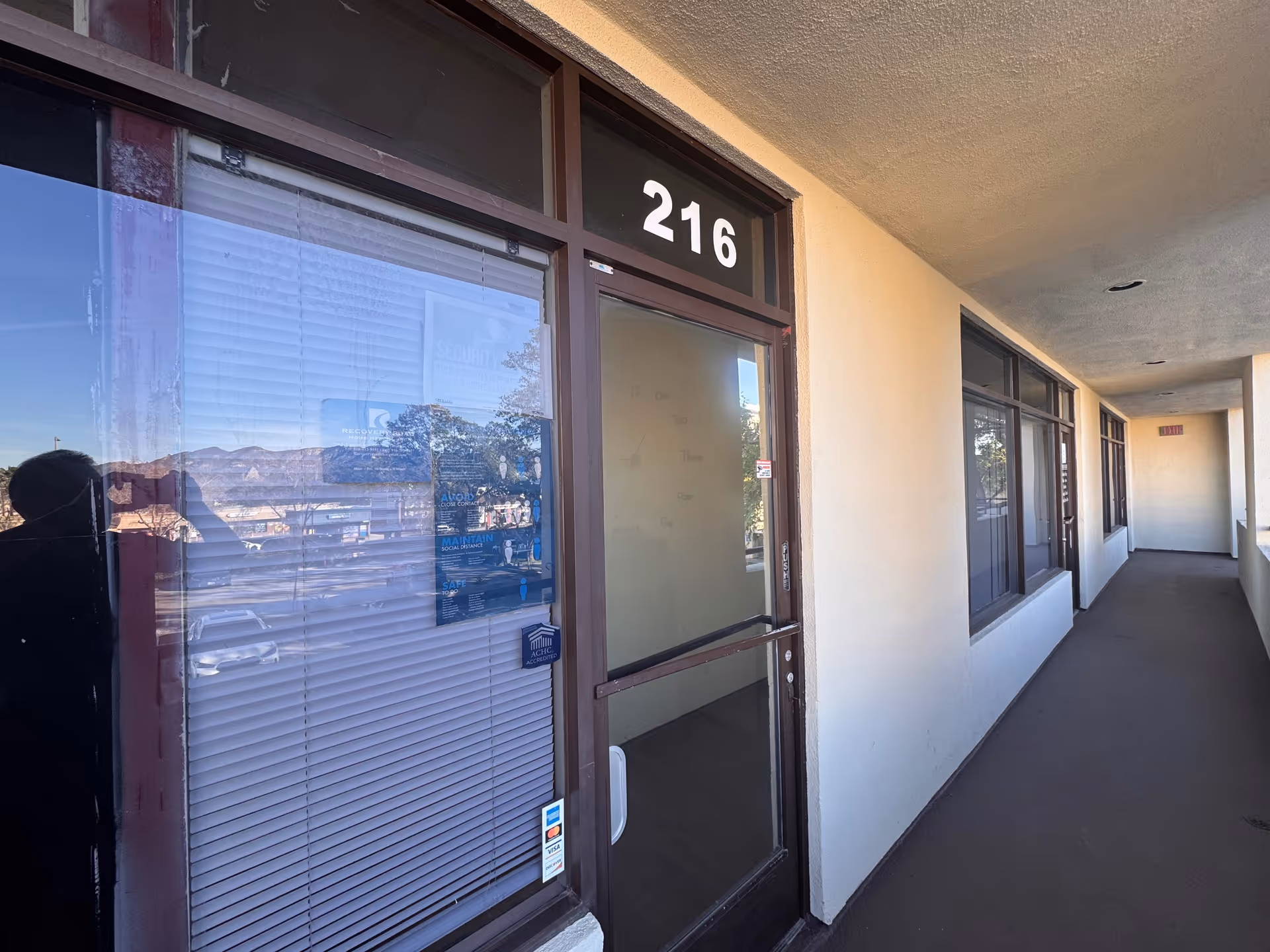 Exterior walkway along a beige building with unit door marked 216 and windows.