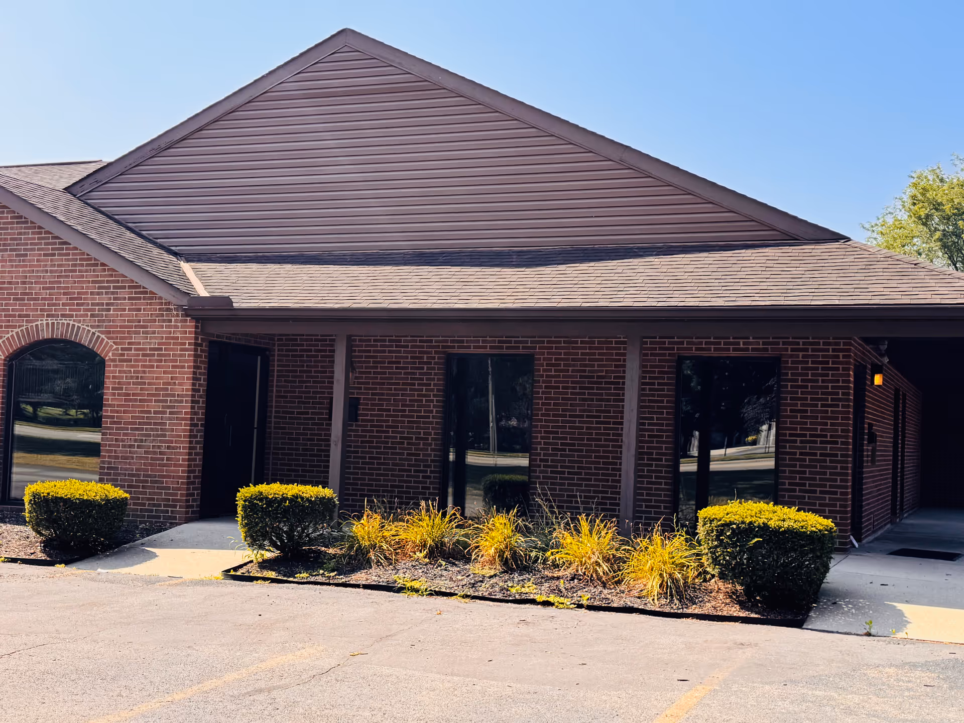 Brick senior living facility entrance with landscaped shrubs and clear blue sky