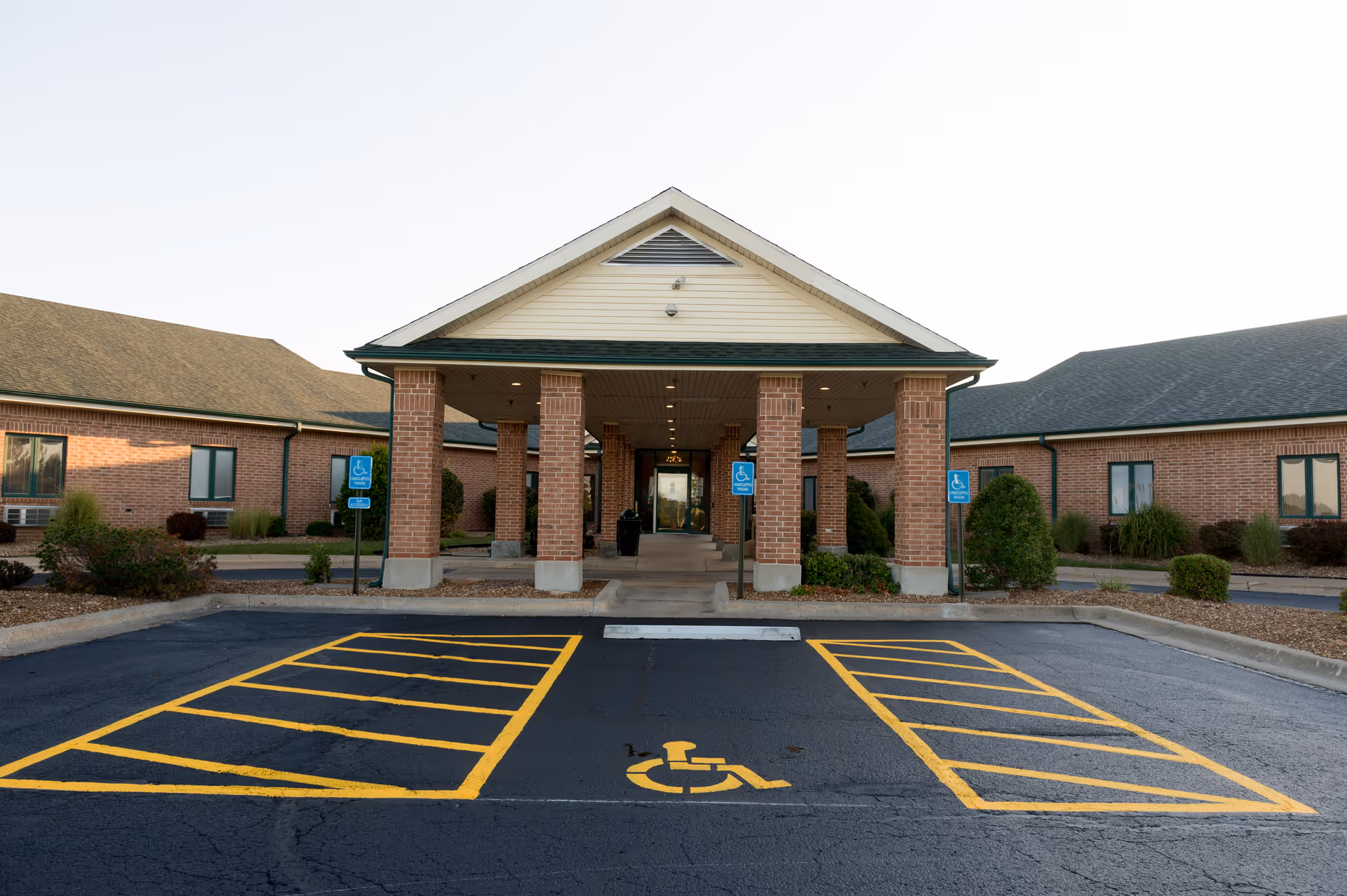 Front view of a brick assisted-living facility with a covered entrance and wheelchair-accessible parking.