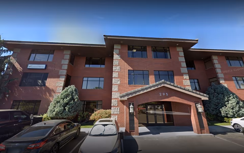 Brick senior living building with glass entrance canopy and parked cars in front.