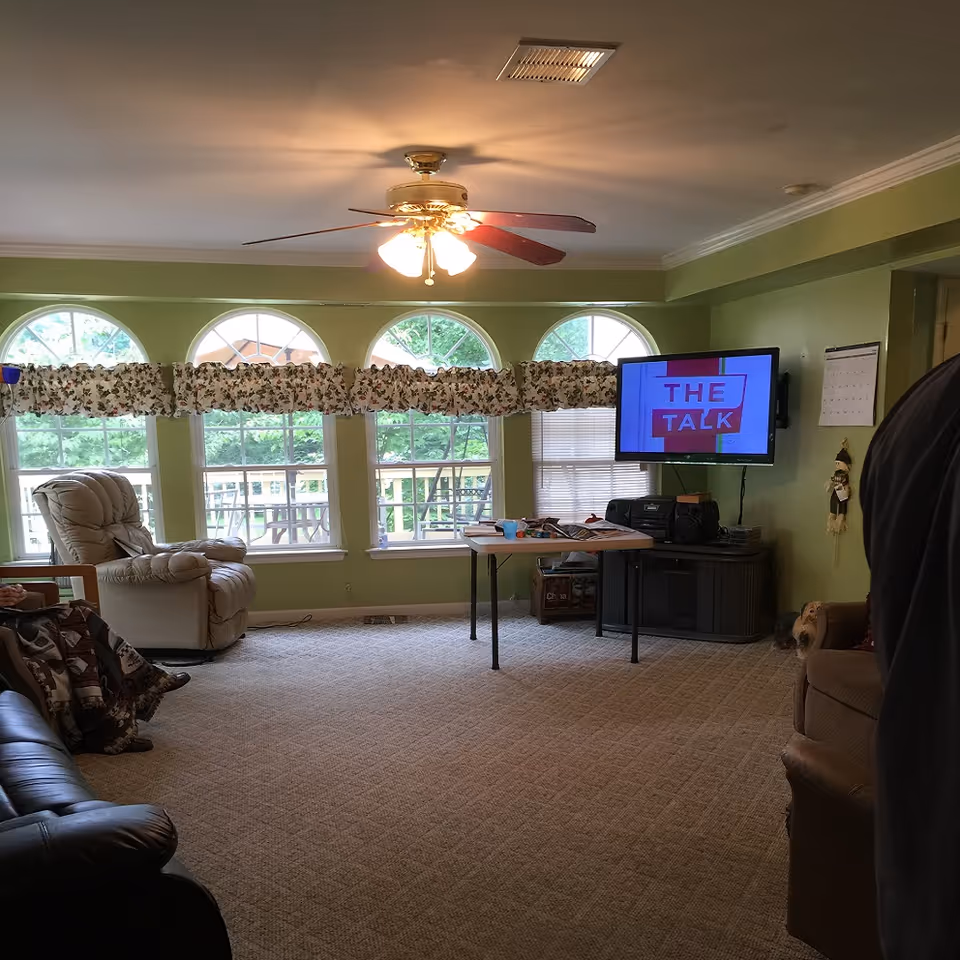 Common living room in a senior care facility with TV, ceiling fan, and seating.