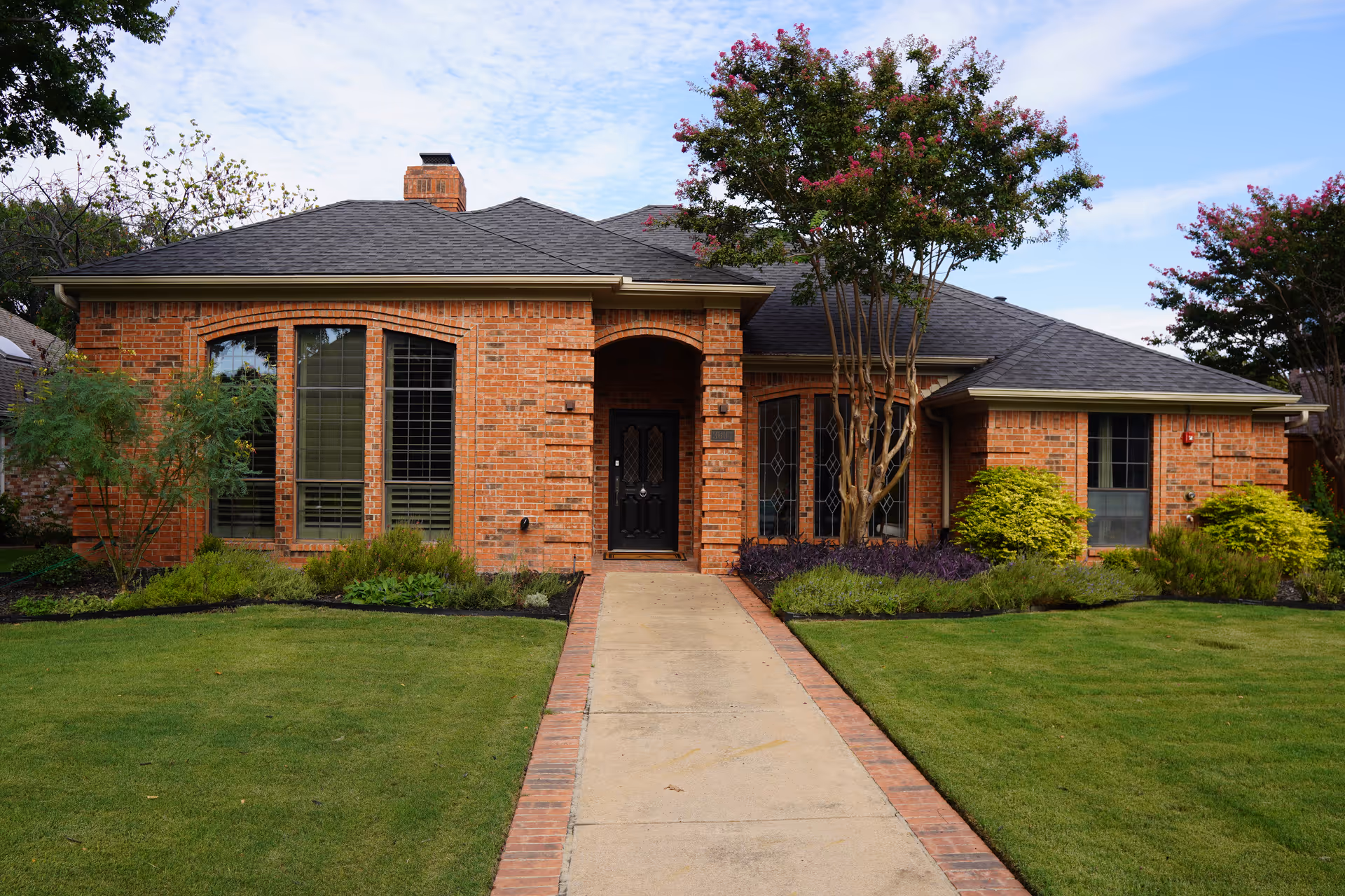 Brick senior living facility exterior with a central entrance, manicured lawn, and walkway.