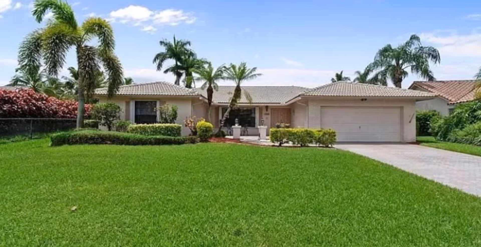 Single-story ranch-style home with a large green lawn, palm trees, and a two-car garage.