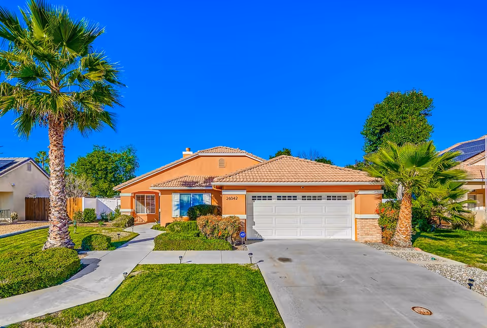 Front exterior of a single-story orange home with a two-car garage and palm trees.